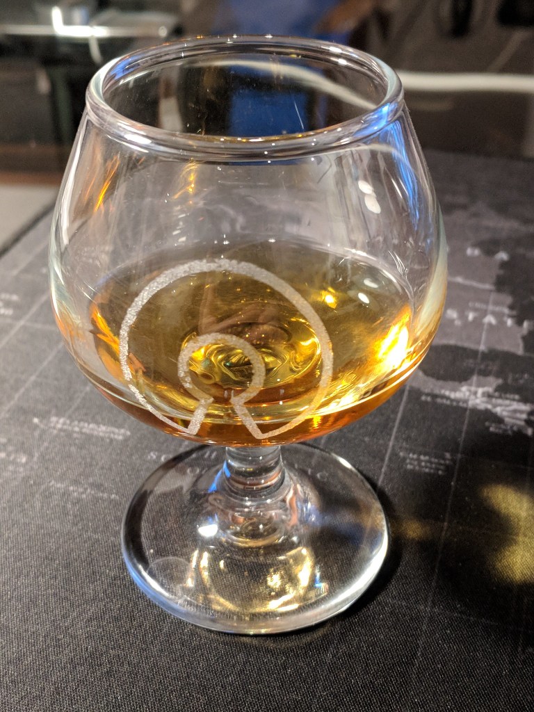 Glass with engraved OSI logo containing distilled spirits